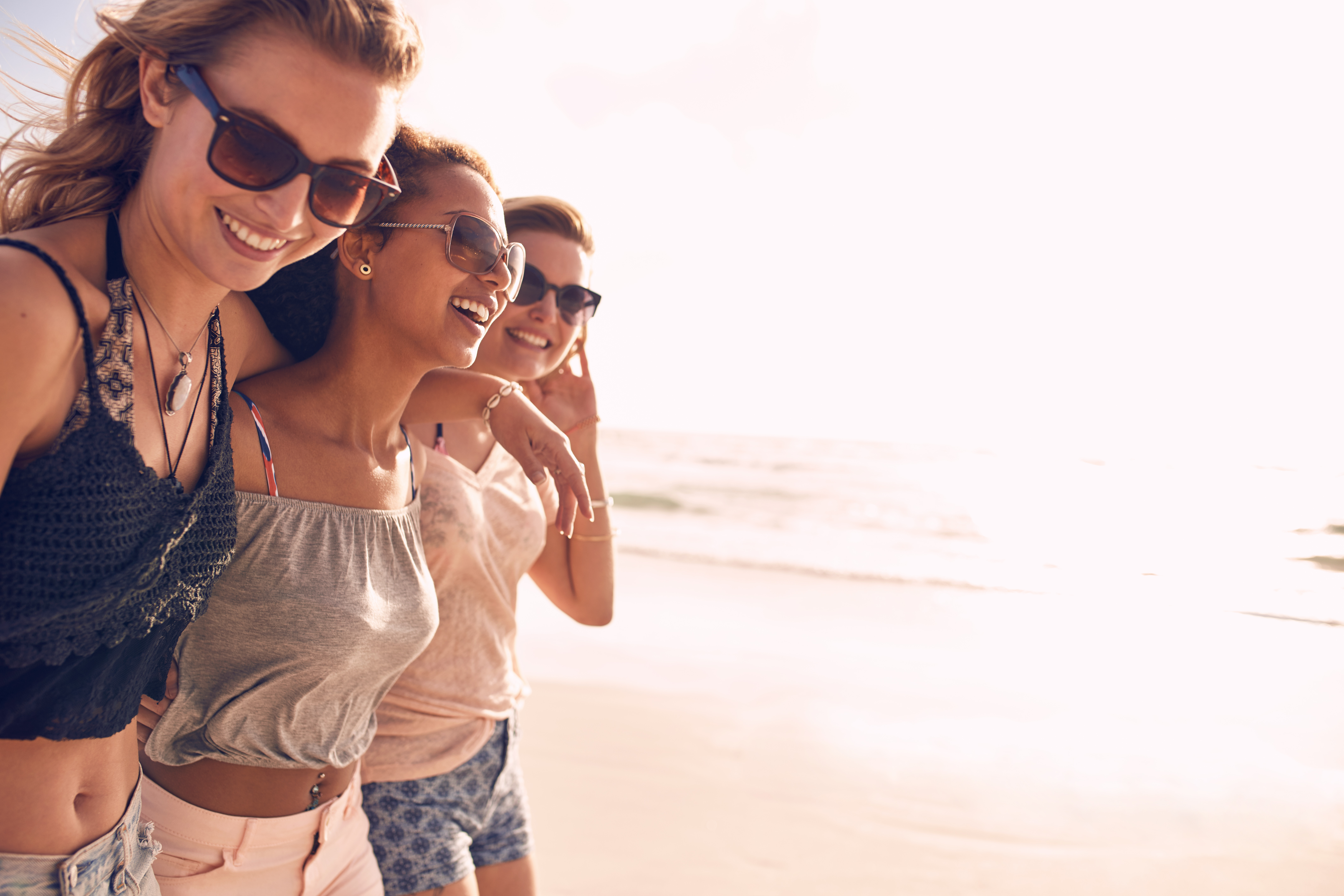 Drie jonge vrouwen lachen samen tijdens een wandeling langs een zonnig strand