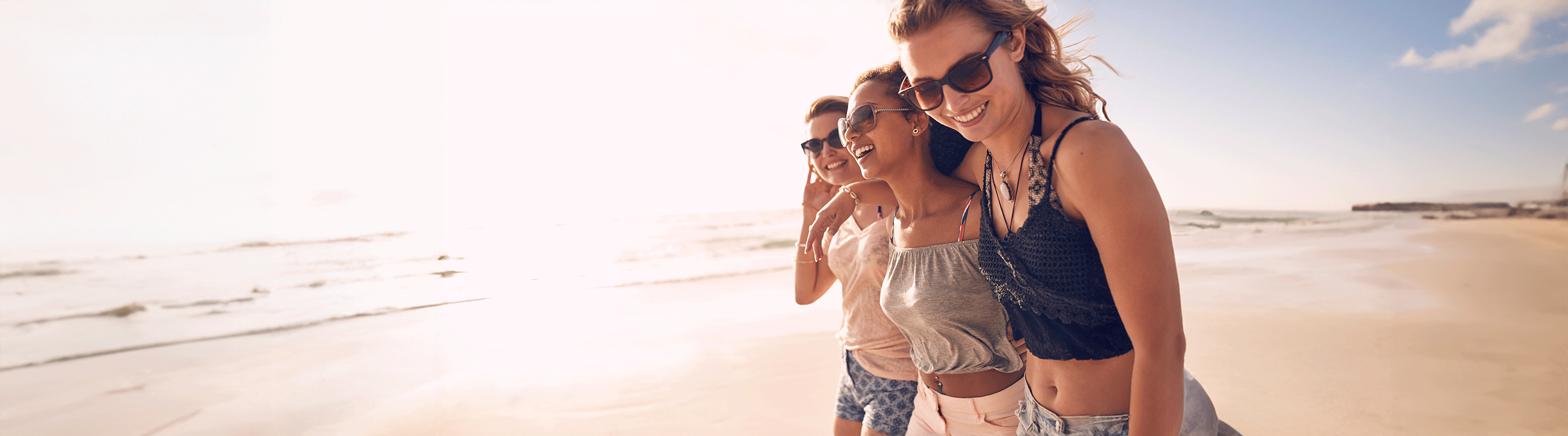 Drie jonge vrouwen lachen samen tijdens een wandeling langs een zonnig strand